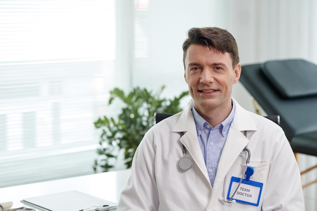 Portret van een glimlachende plastische chirurg in een witte labjas die in het kantoor van de kliniek staat