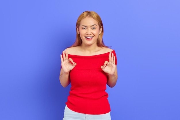 Portret van een glimlachende positieve Aziatische vrouw die zich voordeed en een goed gebaar maakt geïsoleerd op een paarse achtergrond
