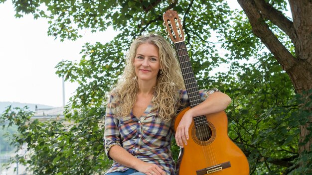 Foto portret van een glimlachende vrouw die met een gitaar tegen bomen zit