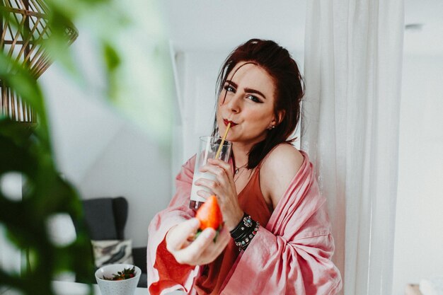 Portret van een glimlachende vrouw die thuis melk drinkt