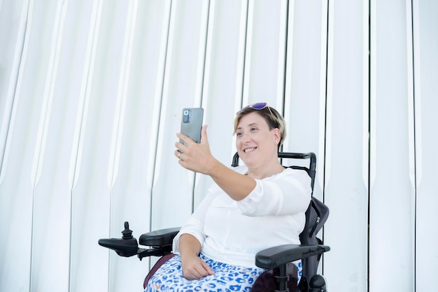 Portret van een glimlachende vrouw met een handicap in een rolstoel die een selfie-foto maakt op een witte achtergrond