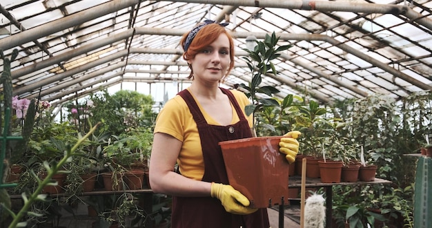 Portret van een glimlachende vrouw met een potplant in een kas