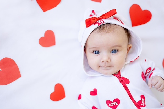 Foto portret van een grappig babymeisje met rode hartjes op een bed op een wit katoenen bed glimlachend of lachend valentijnsdagconcept