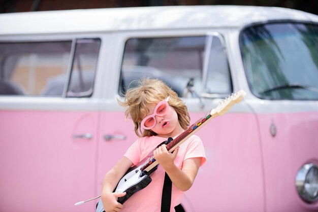 Portret van een grappig kind met een roze bril die een lied oefent tijdens een gitaarles op straat Muziekconcept kindermuziekschool Rockconcert