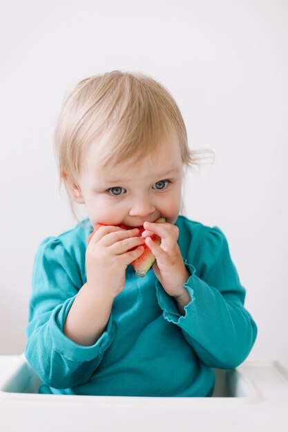 Portret van een grappig klein babymeisje dat in een kinderstoel zit en watermeloen eet