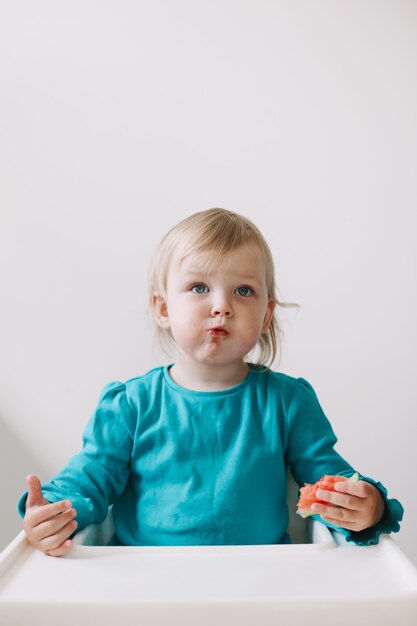 Portret van een grappig klein babymeisje dat in een kinderstoel zit en watermeloen eet