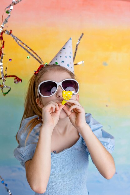 Foto portret van een grappig meisje met een verjaardagshoed en heldere confetti op een gele achtergrond