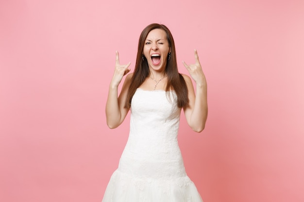 Portret van een grappige gekke vrouw in een witte jurk die staat te knipperen en een rock-n-roll-teken toont