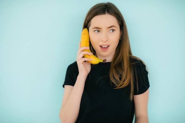 Portret van een grappige vrouw die een bananentelefoon belt op een blauwe achtergrond