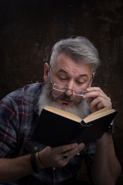 Portret van een grijs-haired bebaarde man met bril lezen boek