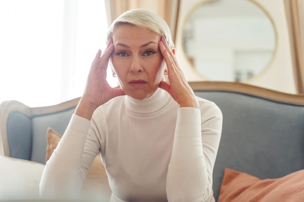 Portret van een grijsharige vrouw met een droevige uitdrukking die haar slapen met vingers aanraakt