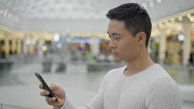 Portret van een hamdsome aziatische man scrollende telefoon op grote winkelcentrum achtergrond