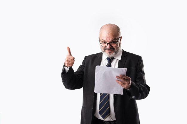 Portret van een Indiase Aziatische senior zakenman die papieren documenten vasthoudt of leest terwijl hij tegen een witte achtergrond staat