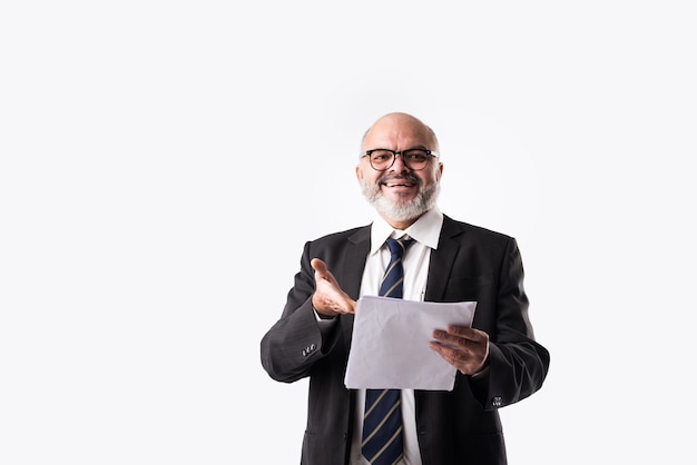 Portret van een Indiase Aziatische senior zakenman die papieren documenten vasthoudt of leest terwijl hij tegen een witte achtergrond staat