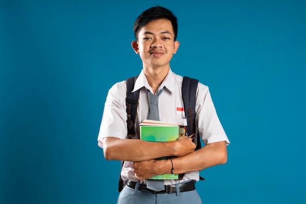 Portret van een Indonesische middelbare schoolstudent die lacht naar de camera met een boek op een blauwe achtergrond