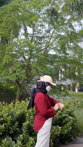 portret van een Indonesische moslimvrouw die een rood-witte jurk draagt en op haar horloge kijkt