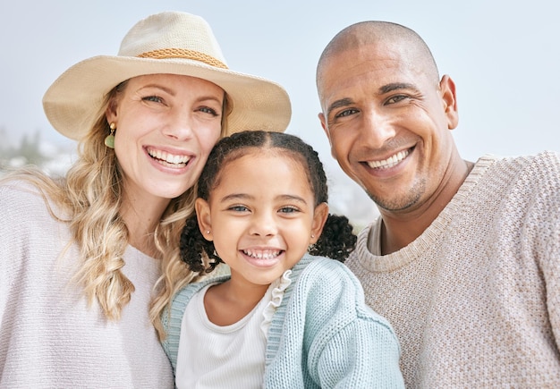 Portret van een interraciale gelukkige familiebinding terwijl ze samen op een strandvakantie zijn Schattig klein meisje omhelst en zit met haar ouders buiten te genieten van frisse zomerlucht met copyspace