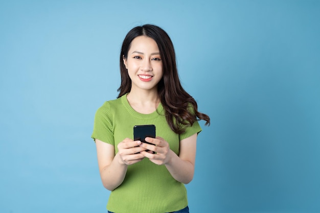Portret van een jong Aziatisch meisje, met telefoon, geïsoleerd op blauwe achtergrond