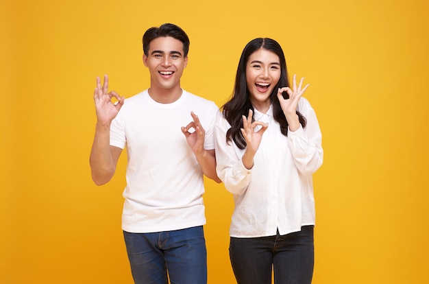 Portret van een jong Aziatisch paar dat ok teken toont dat op gele achtergrond wordt geïsoleerd