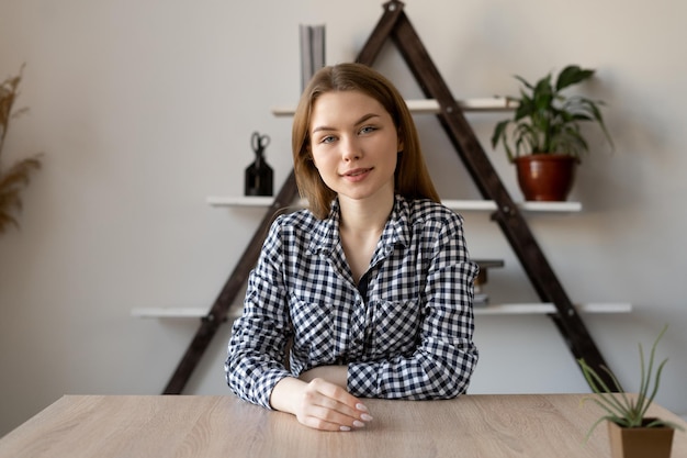 Portret van een jong blank meisje dat aan een tafel zit, naar de camera kijkt en spreekt Online consult