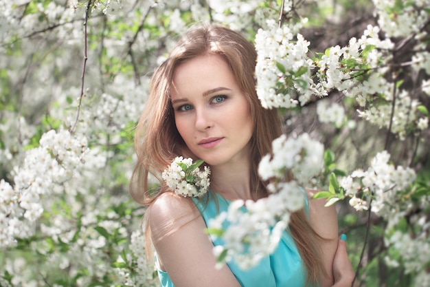 Portret van een jong blond meisje in een blauwe jurk. appelbomen in bloemen.