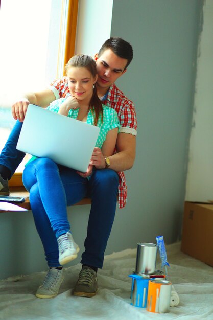 Foto portret van een jong echtpaar dat in een nieuw huis verhuist en met een laptop zit