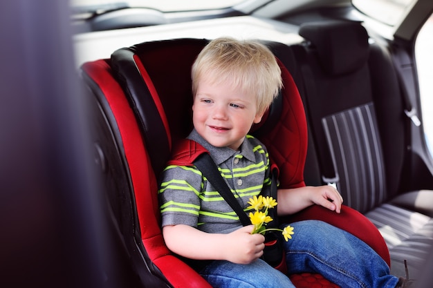 Portret van een jong kind van een jongen met blond haar in een autostoeltje voor kinderen. veilig vervoer van kinderen in de auto.