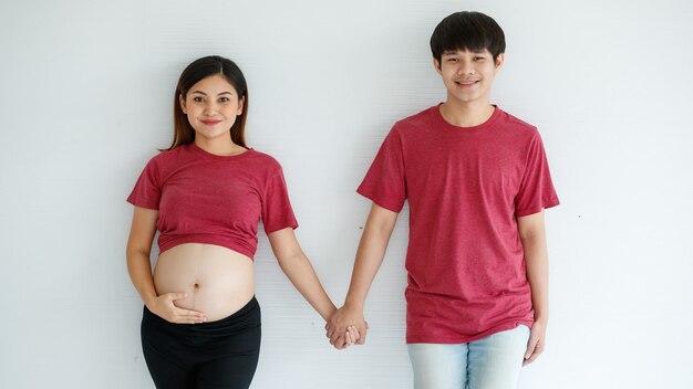 Portret van een jong koppel. Knappe man en zwangere vrouw glimlachend staande hand in hand gelukkig tegen een witte achtergrond. Ze verwachten een gezonde baby.