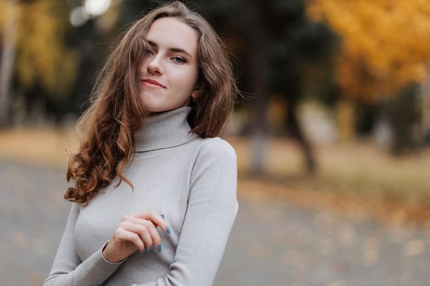 Portret van een jong lachend meisje in een grijze jurk in het herfstpark