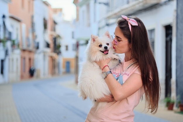 Portret van een jong meisje dat haar witte pluizige pomeranian hond kust.