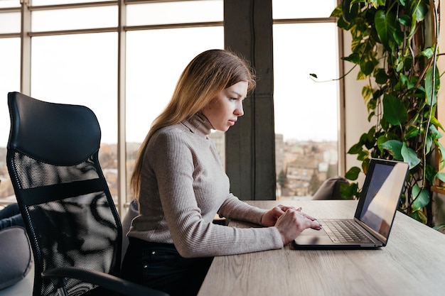 Portret van een jong meisje dat op een laptop werkt en in een moderne coworking-ruimte zit