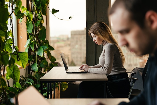 Portret van een jong meisje dat op een laptop werkt en in een moderne coworking-ruimte zit