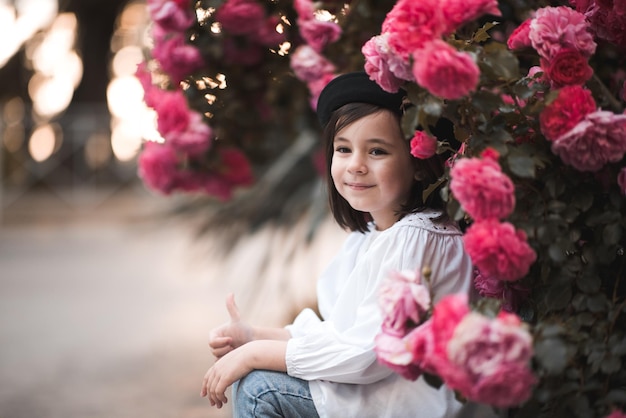 Portret van een jong meisje dat over roze rozen bloemen in de tuin zit