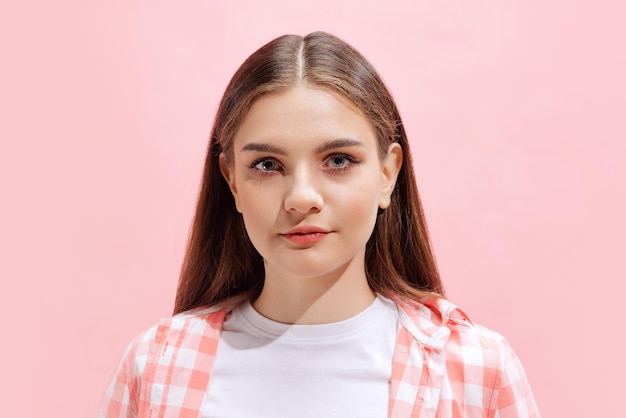 Portret van een jong meisje in geruit hemd poseren geïsoleerd over roze studio achtergrond aandachtig