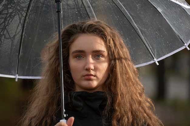 Portret van een jong meisje met lang luxueus bruin golvend haar onder paraplu's op regenachtige herfstdag Verdriet staren