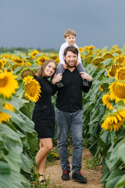 Foto portret van een jong mooi gezin met een klein kind in een veld met zonnebloemen op een zomerdag