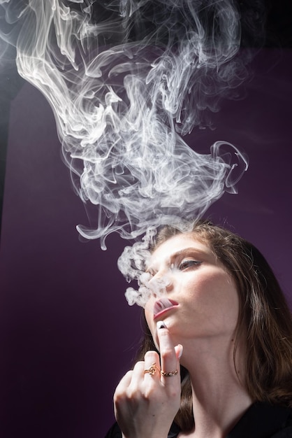 Portret van een jong mooi meisje dat een dikke rook van een adder uitblaast Dramatisch portret op roze achtergrond