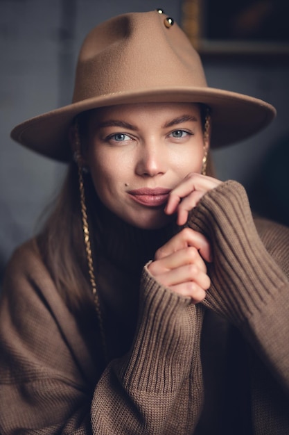 Portret van een jong mooi meisje in een bruine trui en een hoed met een rand