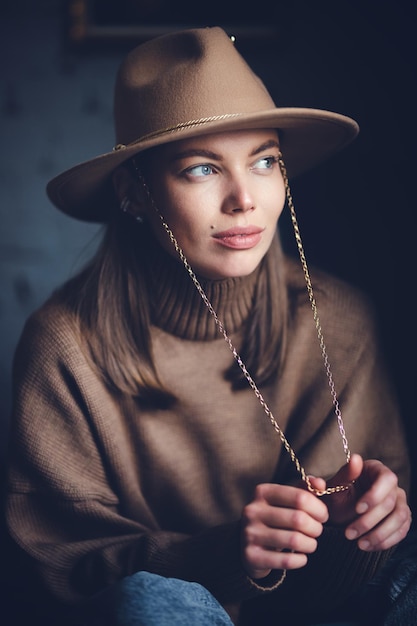 Portret van een jong mooi meisje in een bruine trui en een hoed met een rand