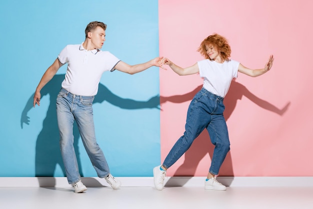 Portret van een jong mooi paar dat vrolijk danst geïsoleerd over roze blauwe studioachtergrond