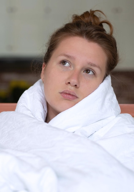 Portret van een jong, ongelukkig, depressief meisje, mooie, luie, eenzame vrouw die zichzelf bedekt met een deken die lijdt aan een depressie met een verdrietige, overstuur gefrustreerde blik thuis in de woonkamer in de vroege ochtend