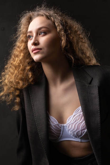 Portret van een jong roodharig krullend sexy meisje in een jas met lang haar in de studio pronkt met haar gewelfde borsten in een beha