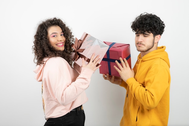 Portret van een jong stel dat cadeaus voor vroege vakantie uitwisselt over witte muur.