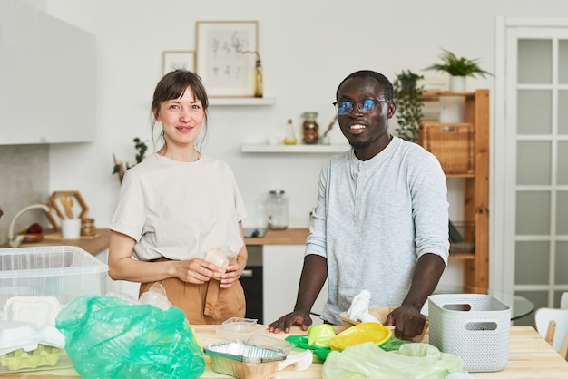 Portret van een jong stel dat naar de camera kijkt terwijl ze het afval in de keuken sorteren