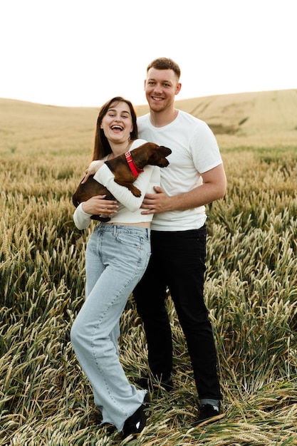 Portret van een jong stel met een huisdier. de man knuffelt het meisje dat de hond vasthoudt. verliefde mensen wandelen langs het veld met een hond.liefhebbers met een hond