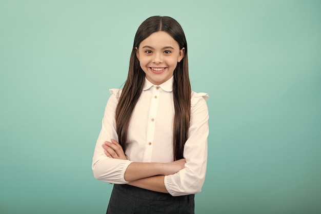 Portret van een jong tienermeisje dat met gekruiste armen staat tegen een blauwe achtergrond met kopieerruimte