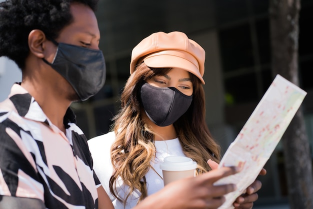 Portret van een jong toeristenpaar dat beschermend masker gebruikt en kaart bekijkt terwijl het buitenshuis op zoek is naar richtingen