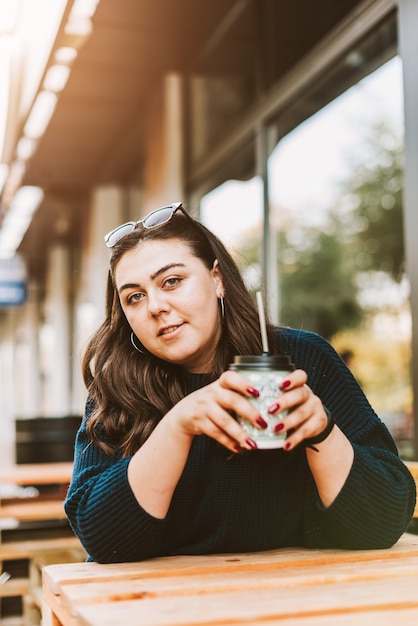 Portret van een jong volwassen meisje met een kopje koffie in de buurt van een café bij goed herfstweer