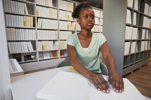 Portret van een jonge afro-amerikaanse vrouw die brailleboek leest in de kopieerruimte van de universiteitsbibliotheek