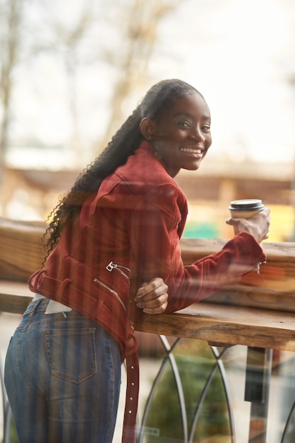 Portret van een jonge Afro-Amerikaanse vrouw die op straat loopt en een kopje koffie in de buitenlucht vasthoudt